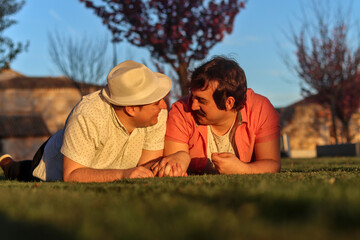 Couple of gay men lying on the grass looking at each other, normal people, front view. LGBT couple...
