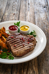 Grilled beef sirloin steak with baked potatoes on wooden table
