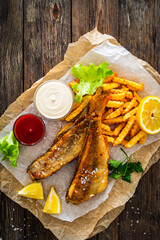 Fried perch with French fries and lemon served on paper on wooden table

