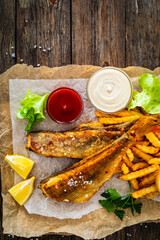 Fried perch with French fries and lemon served on paper on wooden table
