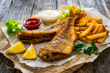 Fried perch with French fries and lemon served on paper on wooden table

