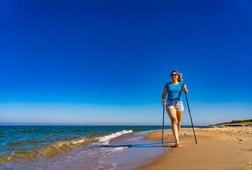 Nordic walking - beautiful woman exercising on beach

