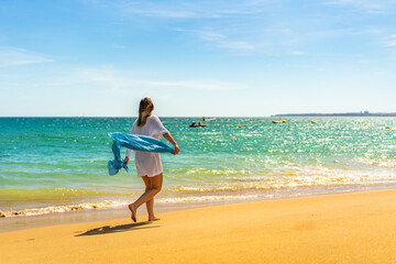 Fototapeta na wymiar Beautiful woman walking on sunny beach holding shawl 
