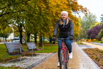 Mid-adult woman riding bicycle in city park on a rainy day
