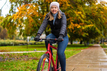 Naklejka premium Mid-adult woman riding bicycle in city park on a rainy day 