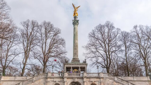 Front view of famous Peace Column with golden Angel of Peace statue (Friedensengel) timelapse, people and public park in the Bavarian capital near Isar river. Germany, Munich, Bogenhausen