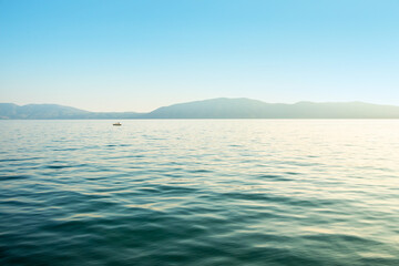 Seascape: sea with gentle waves and a distant shore under the blue sky - obrazy, fototapety, plakaty