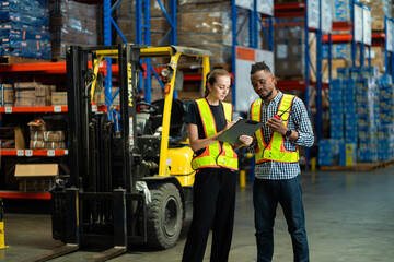 Two people are standing in a warehouse, one of them is holding a clipboard. The warehouse is filled...