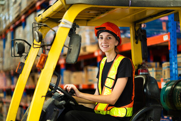 A woman is driving a forklift in a warehouse. She is wearing a safety vest and a hard hat