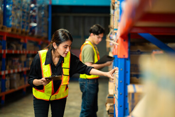Two workers in a warehouse, one of them is checking a box. The woman is wearing a safety vest and a...