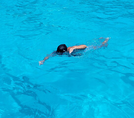 Woman with black cap swimming in a pool of blue water