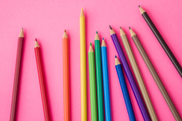 Colorful pencils scattered playfully on a vibrant pink background.