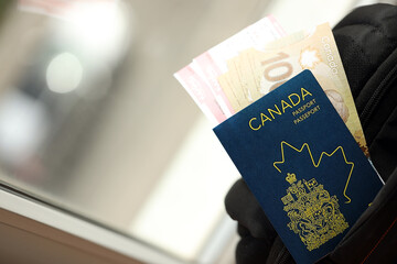Canadian passport and dollar money bills with airline tickets on backpack close up