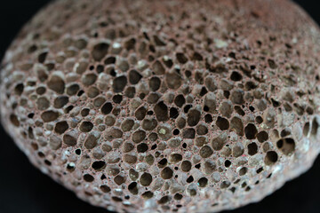 Dark pumice stone with visible irregularities in a circular shape.
