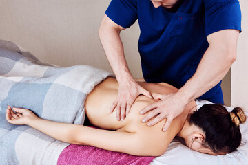 Massage therapist presses with both hands on woman back in shoulder area during deep tissue massage...