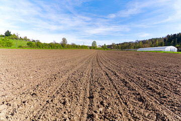 Diminishing view of freshly ploughed agriculture field at farm with white greenhouse in the background on a sunny spring day. Photo taken April 13th, 2024, Zurich, Switzerland.