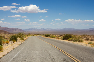 Fototapeta na wymiar Two lane road through Joshua Tree National Park, California, USA with view of blue sky and mountains