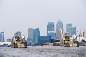 Two of the Futuristic looking steel-clad shells of the Thames barrier with the high rise buildings of Canary wharf, greater London, UK, on the horizon in the background
