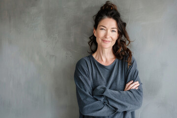 Fototapeta premium Portrait of a smiling confident woman in her forties, with crossed arms in front of a grey wall background