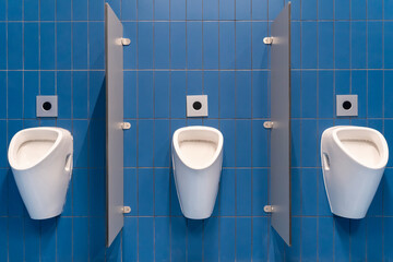 A row of urinals in a blue-tiled public toilet