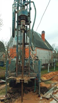 Boring the well with the help of special machinery. Drilling equipment producing the water bore. Private cottage at backdrop. Vertical video.