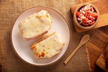 Molletes. Mexican recipe based on bolillo bread split lengthwise, spread with refried beans and gratin cheese, adding pico de gallo sauce and some protein such as ham, bacon or chorizo. - 783962241