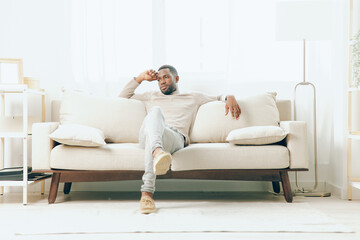 Thoughtful African American Man Sitting on Sofa, Reflecting on a Relaxing Home Life and...