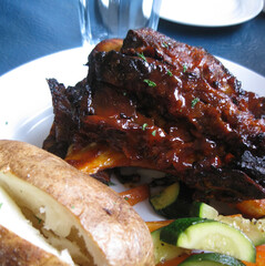 Barbecued beef ribs served with a baked potato and saut&eacute;ed vegetables.