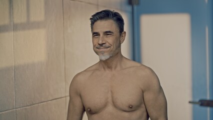 Confident mature male standing shirtless in front of a bathroom mirror. Portrait of muscular fit aged man, smiling. - 783963414