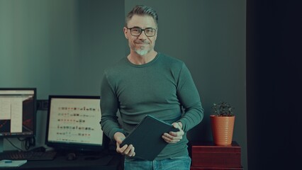 Older man working with tablet computer in home office. Mid adult male in glasses, happy, smiling, looking at camera. Casual entrepreneur, businessman in office.