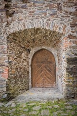 Old wooden door in an old stone wall with arches in a medieval castle