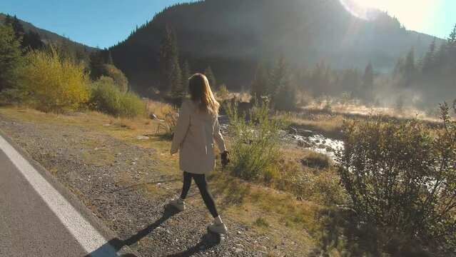 Tourist blogger woman walking on mountain road on sunset. Joyful girl having adventure in mountains.
