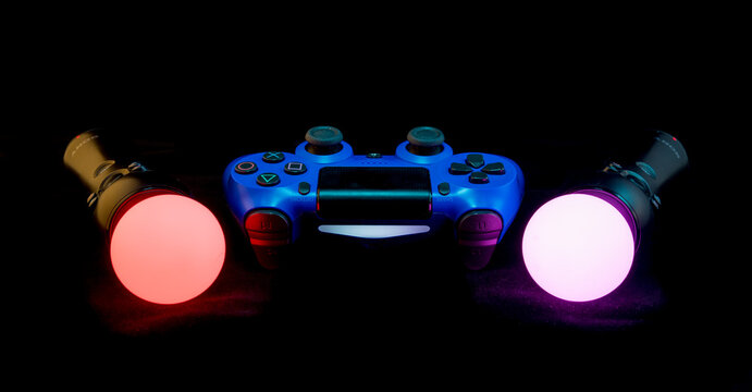 Blue Playstation 4 controller with Move controllers lit up against a black background. London - 22nd April 2020