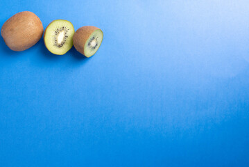 Kiwi fruit, one whole, one sliced in half on a bright blue background.