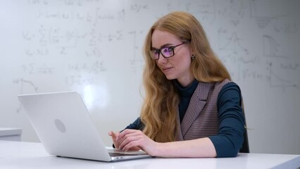 Caucasian woman scientist typing on laptop. White board with formulas.  - Powered by Adobe