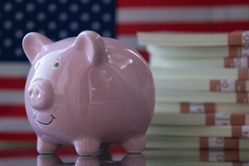PClose up pink piggy bank with US Dollar bills against flag of United States as symbol of economy, business and investment of USA. Copy space.