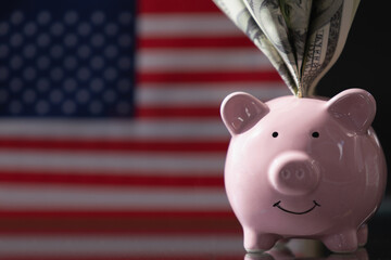Pink piggy bank with US Dollar bills against flag of United States as symbol of economy, business and investment of USA. Copy space.
