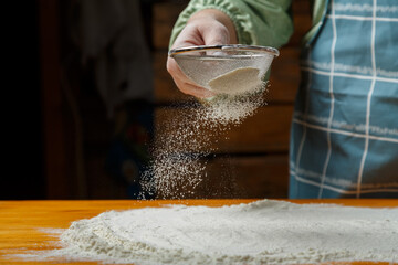 A woman holds a sieve and sifts flour over the table. Horizontal