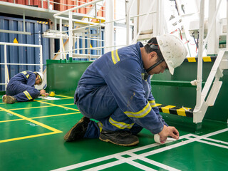 Seaman crew member of cargo vessel  equipped with personal protective equipment is painting vessel deck with signal color paint