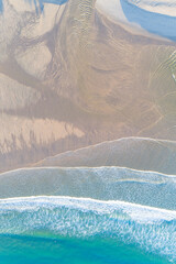 aerial drone overhead view of the waves of a turquoise sea arriving at the shore of a beach in...