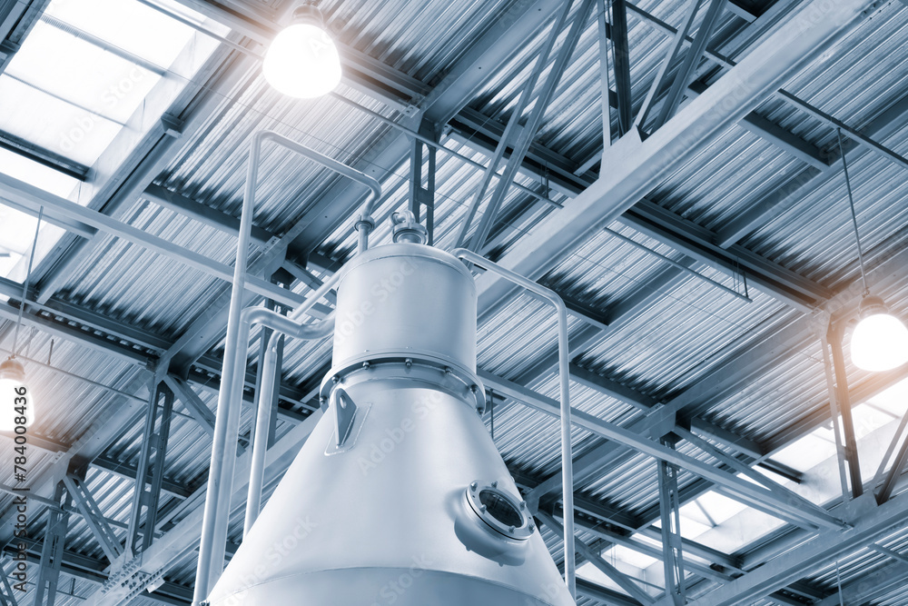 Poster A large industrial building with a large silver tank on top. The tank is surrounded by a metal frame and is located in the middle of the building. The building is lit up with bright lights