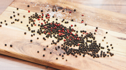 A wooden cutting board with a pile of red, black, and white pepper flakes. Concept of abundance and...