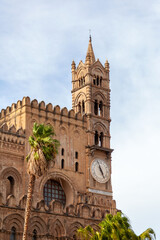 Fototapeta na wymiar Bell tower of Palermo Cathedral, framed by a palm tree against a blue sky, showcasing its historic clock