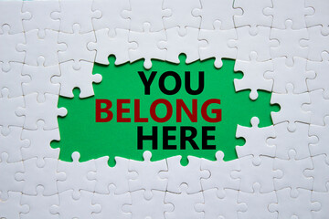 You belong here symbol. White puzzle with words You belong here. Beautiful green background. Business and You belong here concept. Copy space.