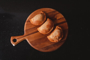 Overhead view of some freshly fried empanadas on a round wooden tray.