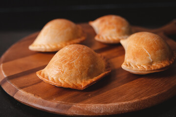 Detail view of some freshly baked empanadas on top of a round wooden tray.