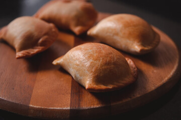 Detail view of a baked empanada on a circular wooden tray.