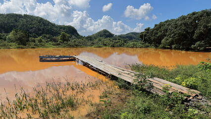 Muddy pond with a wooden plank pontoon for the berthing of a schematic, home-made rowboat in the Valle del Silencio Valley area. Viñales-Cuba-173