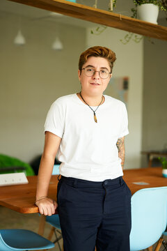 Transgender professional stands confidently in office, showcasing inclusivity in modern workplace. Smart casual attire, positive ambiance, and corporate setting reflect progressive business values.
