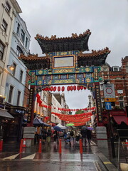 London, UK - 10.02.2021: Pedestrians with umbrellas walking under the colourful Chinatown Gate...